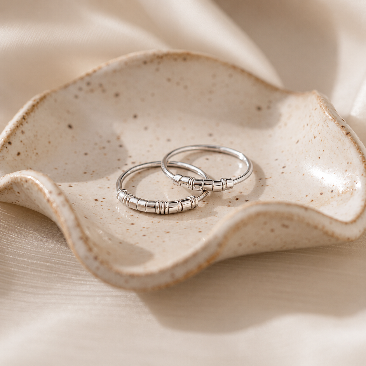 Two silver rings on a textured ceramic dish with a neutral background
